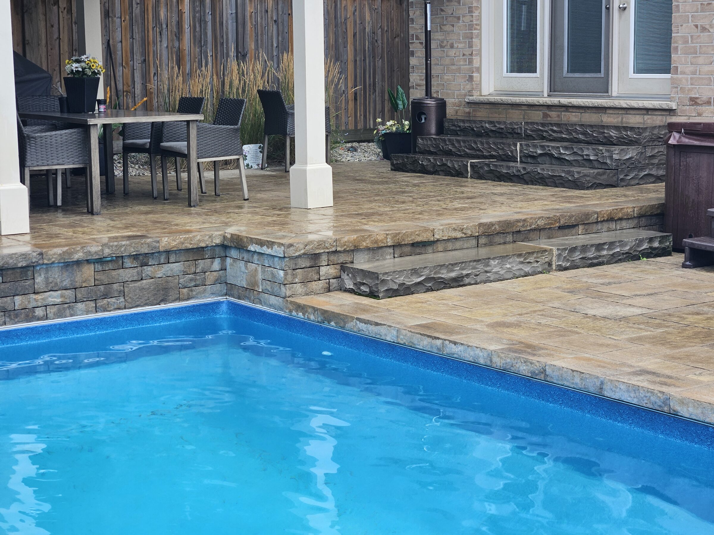 The image depicts a backyard patio with a pool, outdoor dining area, plants, and stone steps leading to a house.