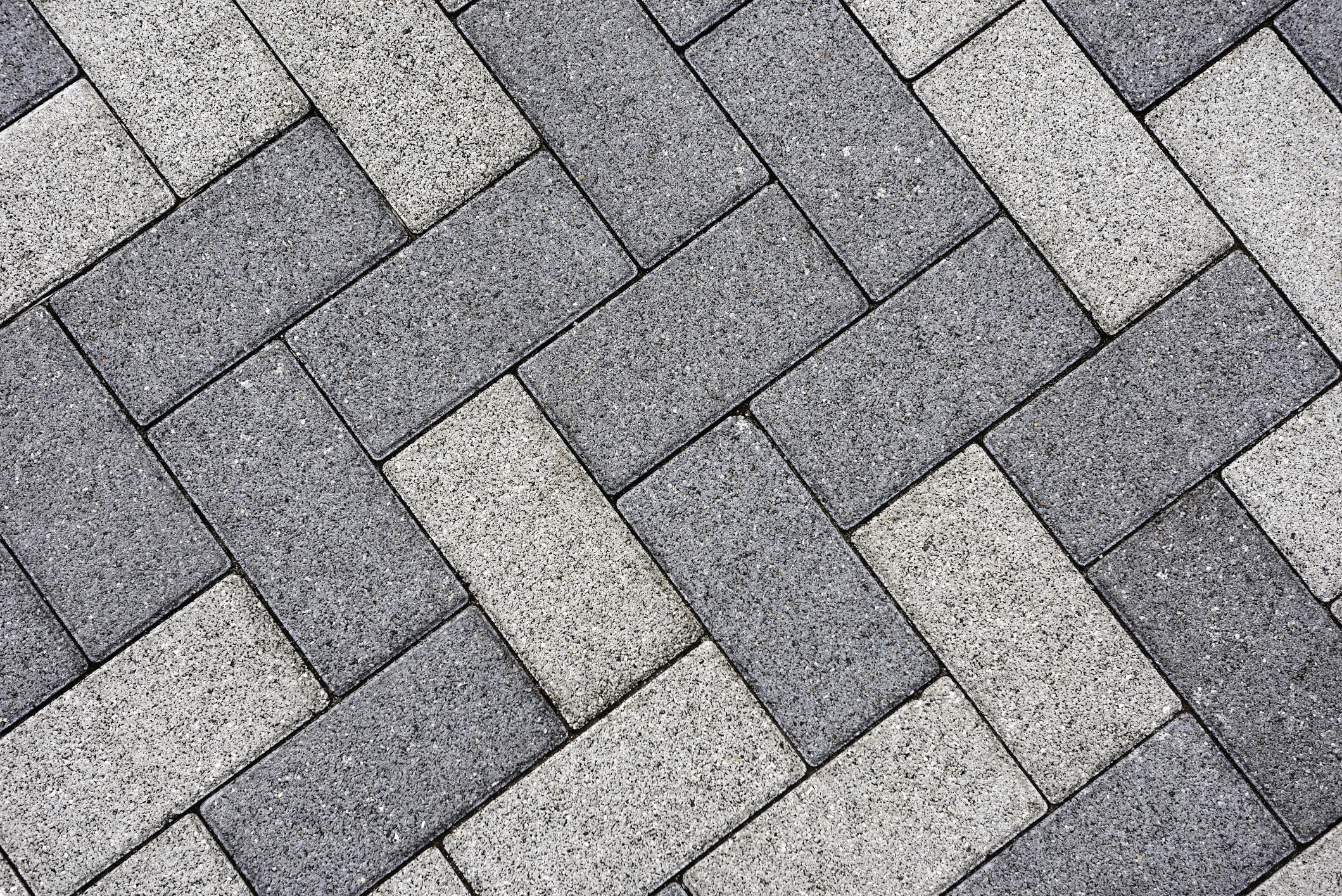 Close-up of a herringbone pattern made of interlocking gray and white rectangular bricks on a paved surface.