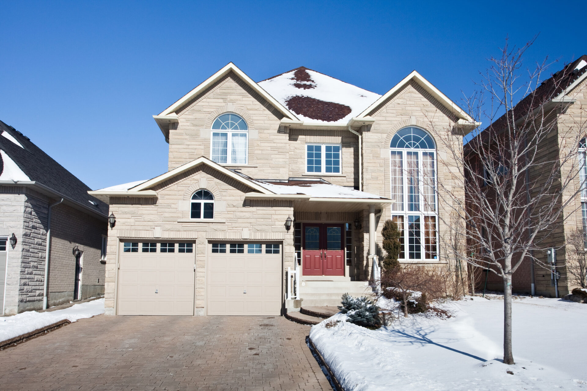 A two-story house with red doors and large windows, surrounded by snow, under a clear blue sky, no recognizable landmarks or historical buildings visible.